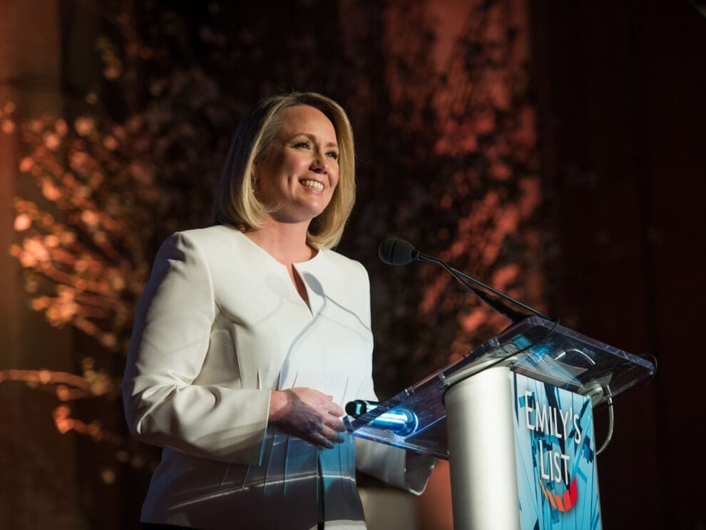 Image of Stephanie Schriock, former president of EMILYs List, speaking at a podium.